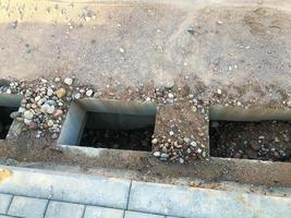 hay agujeros especiales en el asfalto para colocar futuras aguas residuales. preparación para la creación de un sistema de drenaje de agua. sin rejillas, de arena con piedras. el agua circula por los agujeros foto