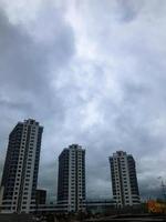 three new, unusual and tall apartment buildings in the city. against the backdrop of a cloudy rainy blue sky. next to a playground with different entertainment. bright new courtyard photo