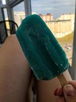girl with turquoise ice cream in her hands sits on the balcony against the background of sunset. beautiful view of the city from the high floor. ice cream with ice and snow. fruit ice photo