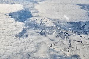 Aerial cloudscape view over clouds top to snow covered rivers, roads, cities and fields, winter air photo