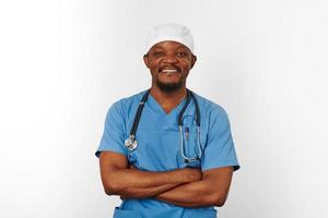 sonriente médico cirujano negro barbudo con abrigo azul y gorra médica con estetoscopio de brazos cruzados foto