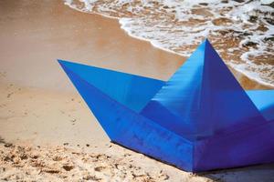 Origami blue paper boat on sandy beach for concept design, beautiful paper ship on shore, close up photo