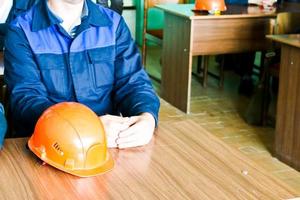 un hombre que trabaja como ingeniero con un casco amarillo naranja sobre la mesa está estudiando, escribiendo en un cuaderno en una fábrica de plantas industriales foto