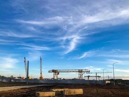 las grúas de construcción se alzan contra el fondo de un cielo azul nublado. sitio de construcción, equipo de excavación de túneles. grúa de pórtico amarilla para el transporte de materiales pesados de hormigón foto