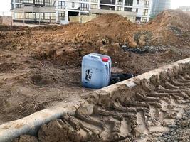 a white construction canister with a red lid is on the ground. the canister is smeared with black viscous and sticky fuel oil. construction site, container for transferring various liquids photo