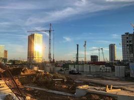 las grúas de construcción están erigiendo nuevas casas a partir de bloques. nuevas construcciones, lugares de vida de las personas. en casas acristalamiento panorámico, donde se refleja el sol del atardecer foto