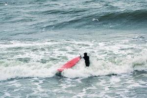 surfista masculino en traje de baño en olas de mar con tabla de surf roja foto