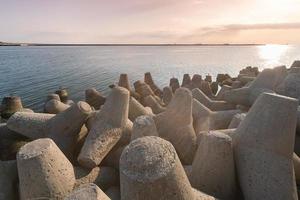 Tetrapod breakwaters in sea water. Beautiful sunset seascape with concrete tetrapodes for protect coastal structures from storm sea waves, effects of weather and longshore drift photo