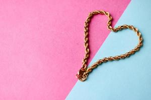 textura de una hermosa cadena festiva dorada tejido único en forma de corazón sobre un fondo azul púrpura rosa y espacio de copia. concepto amor, propuesta de matrimonio, matrimonio, st. día de San Valentín foto