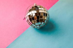 Silver mirror musical club disco ball small round glass winter shiny decorative beautiful xmas festive Christmas ball, Christmas toy plastered on glitter on a gray pink purple background photo