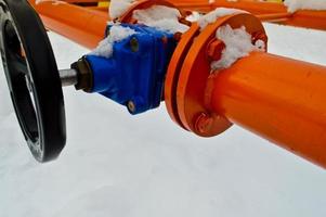 Industrial shut-off regulating protective pipe fittings. Black valve for opening, closing on an iron orange metal pipe with flanges, studs, nuts against the background of white snow in winter photo