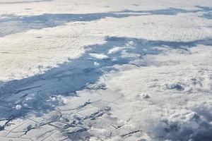 Aerial view over clouds top to snow covered rivers, fields and roads, winter fresh frosty air photo