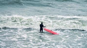 surfista masculino en traje de baño en olas de mar con tabla de surf roja foto