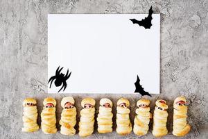 Scary sausage mummies in dough with funny eyes on table. Mockup decoration. Halloween food. Top view. Flat lay photo