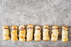 Scary sausage mummies in dough with funny eyes on table.  Halloween food. Top view. Flat lay photo