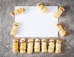 Scary sausage mummies in dough with funny eyes on table. Mockup decoration. Halloween food. Top view. Flat lay photo