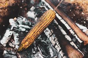 el maíz amarillo se asa a la parrilla sobre carbones abiertos al aire libre, en primer plano. foto