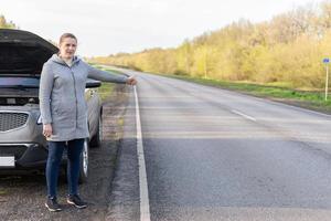 A woman in a jacket is trying to fix a broken car on the road. photo