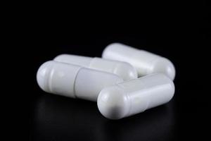 White tablet with two pills in background. Black background with reflection photo