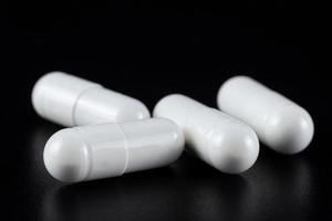 White tablet with two pills in background. Black background with reflection photo