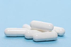 Close up three white gel cap pills of medicine over dark blue background with copy space, elevated high angle view, directly above photo