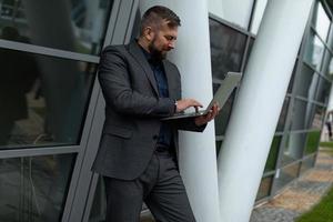 a man in a business suit is typing on a laptop standing next to an office building photo