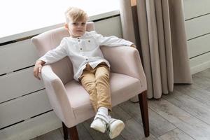 naughty stylish little boy sits in an easy chair and looks at the camera photo
