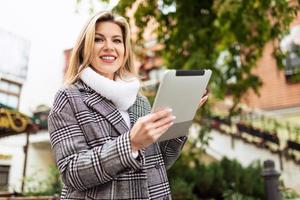businesswoman with a tablet in her hands in an autumn coat with a wide smile on the background of the urban landscape, business and risk insurance concept