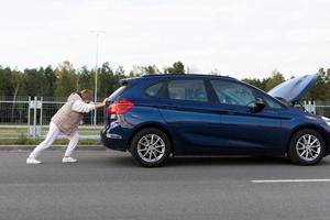 una mujer sola empuja un auto roto en una estación de servicio foto
