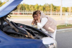 a woman driver in bewilderment, putting her hands to her head, looks at the engine of a broken car photo