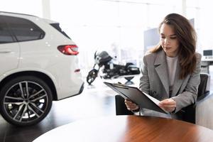 a young woman reads a contract for the purchase of a new car in a car dealership on credit photo