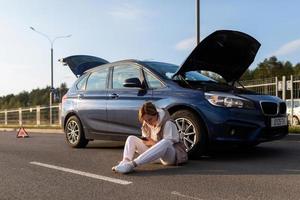 mujer joven esperando ayuda sentada cerca de un camión averiado en la carretera foto