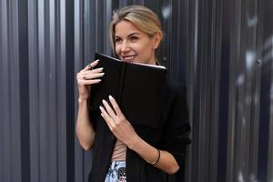 trabajadora de oficina de mediana edad sosteniendo un cuaderno con una sonrisa mirando a la cámara foto