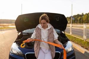 a woman next to a broken car holds a cable with a hook for transporting a car in her hands photo