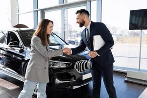 gerente y comprador en un concesionario de automóviles firman documentos sobre la compra de un automóvil nuevo foto