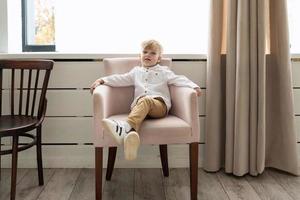 portrait of a little stylish boy sitting in a chair in a white shirt photo