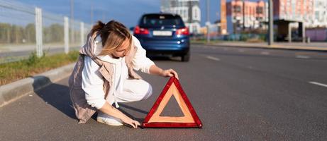 a woman driver puts an emergency stop sign near a broken car, traffic accident concept photo