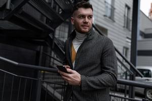 successful businessman entrepreneur in a stylish gray coat and a mobile phone in his hands photo