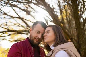 an adult married couple stand to each other against the background of a branchy autumn tree, close-up portrait photo