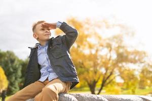 Cheerful mischievous boy in the autumn park looks into the distance with his hand to his forehead photo
