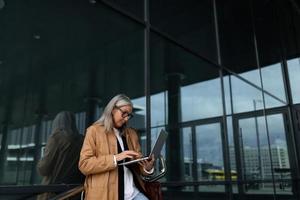 stylish fifty year old woman working on a laptop at the entrance to the office building photo