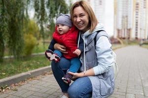 retrato de una joven madre con su hijo de un año en los brazos contra el fondo de un parque de la ciudad foto