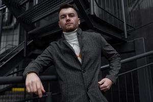 stylish portrait of a brutal man in a coat on the background of a black building photo