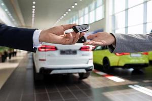 handing over the keys close-up by the seller of the car dealership to the buyer on the background of new cars photo