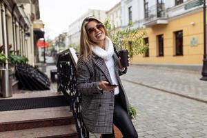 adult Strong woman with a cup of coffee with a mobile phone in her hands looks at the camera with a smile While traveling through the old city photo