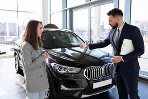 a salesman in a car dealership talks about the benefits of a new SUV to a buyer photo