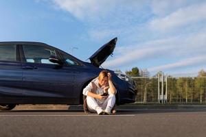 woman driver waiting for help from emergency tow truck near broken down car with open hood photo