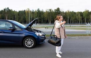 a young woman with a bag on her shoulder votes on the road and looks for a ride next to a collapsed car, transport auto insurance concept photo