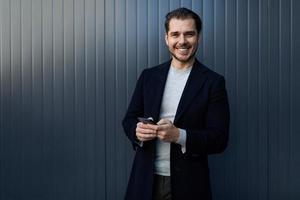 successful young software engineer with a wide smile on his face and a mobile phone in his hands against a gray wall photo