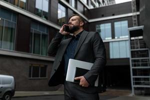 retrato de un hombre de negocios con una laptop hablando por teléfono bien vestido con ropa de negocios en el fondo de un centro de negocios, concepto de un exitoso agente inmobiliario foto